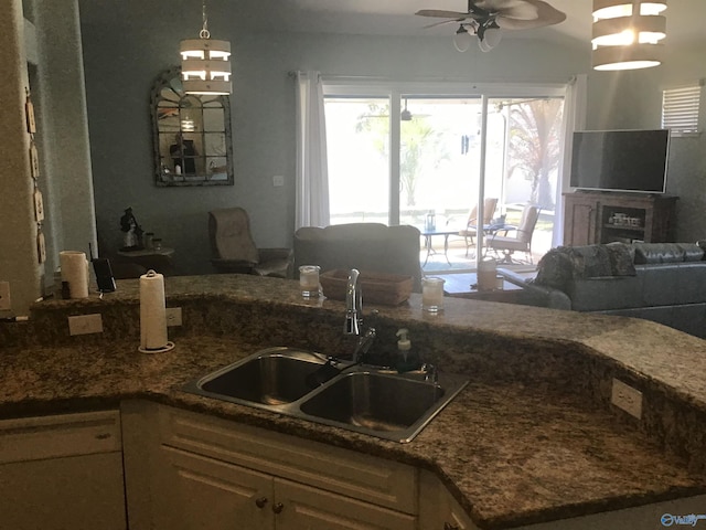 kitchen with a ceiling fan, dark stone counters, a sink, decorative light fixtures, and open floor plan