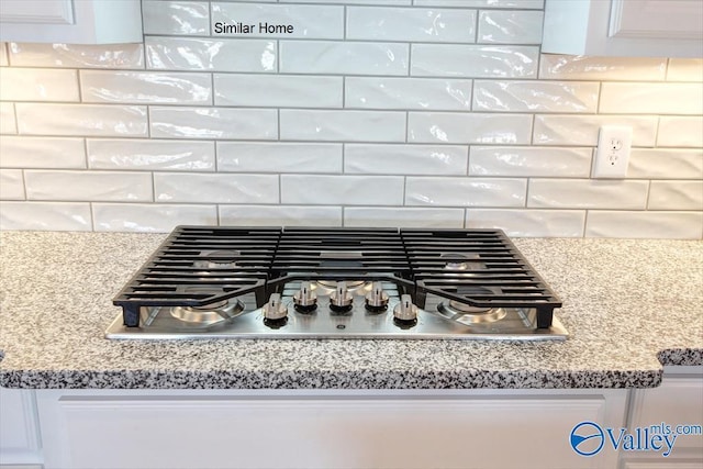 details with white cabinets, decorative backsplash, light stone counters, and stainless steel gas cooktop