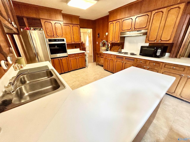 kitchen with light tile patterned flooring, sink, wooden walls, and stainless steel appliances