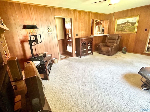 sitting room featuring ceiling fan, wooden walls, and carpet flooring