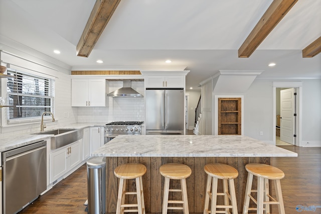 kitchen with wall chimney exhaust hood, appliances with stainless steel finishes, sink, and a kitchen island