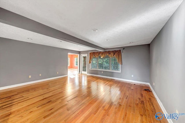 interior space with beamed ceiling, a textured ceiling, and light wood-type flooring