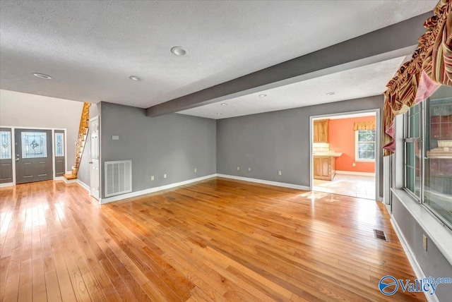 unfurnished living room with beam ceiling, light hardwood / wood-style floors, a textured ceiling, and a healthy amount of sunlight