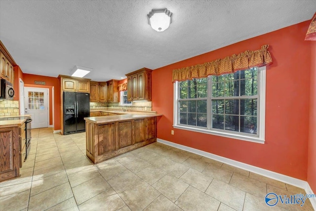 kitchen featuring kitchen peninsula, decorative backsplash, light tile patterned floors, black fridge, and a textured ceiling