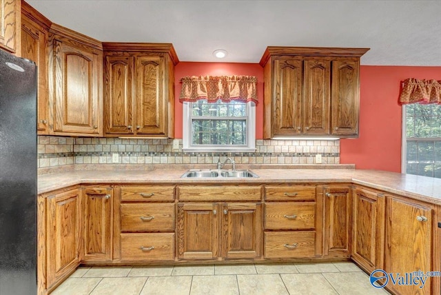 kitchen with sink, light tile patterned floors, backsplash, and black fridge