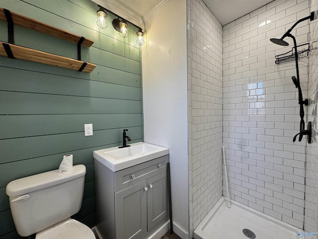 bathroom with tiled shower, toilet, vanity, wooden walls, and ornamental molding