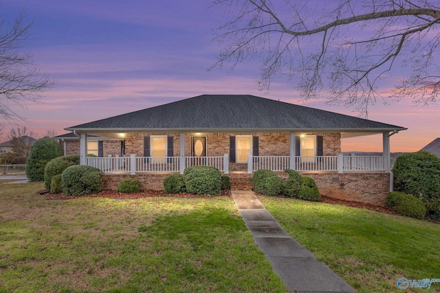 view of front facade featuring a porch, brick siding, a front lawn, and roof with shingles