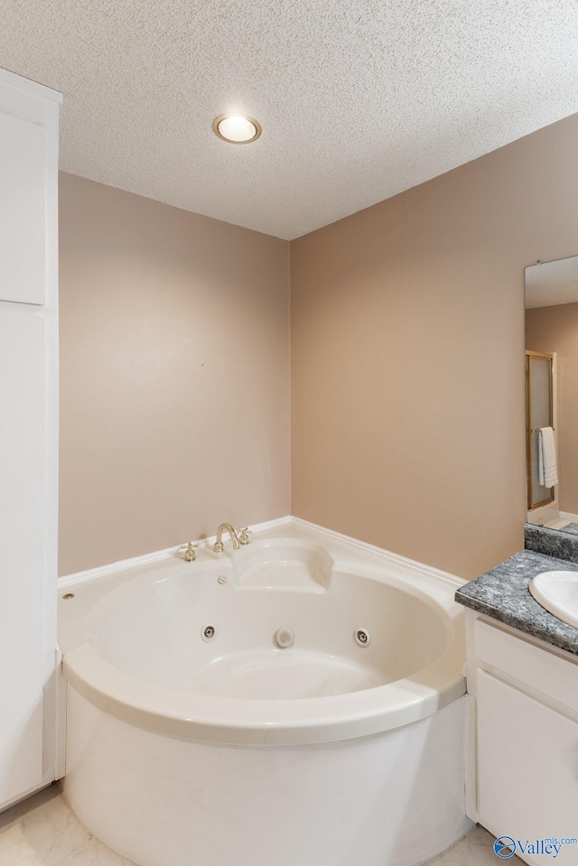 bathroom with vanity, a tub with jets, and a textured ceiling