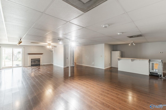 unfurnished living room with baseboards, dark wood-style flooring, ceiling fan, a paneled ceiling, and a tiled fireplace