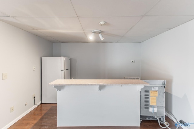 kitchen with dark wood-type flooring, a kitchen breakfast bar, a paneled ceiling, and freestanding refrigerator