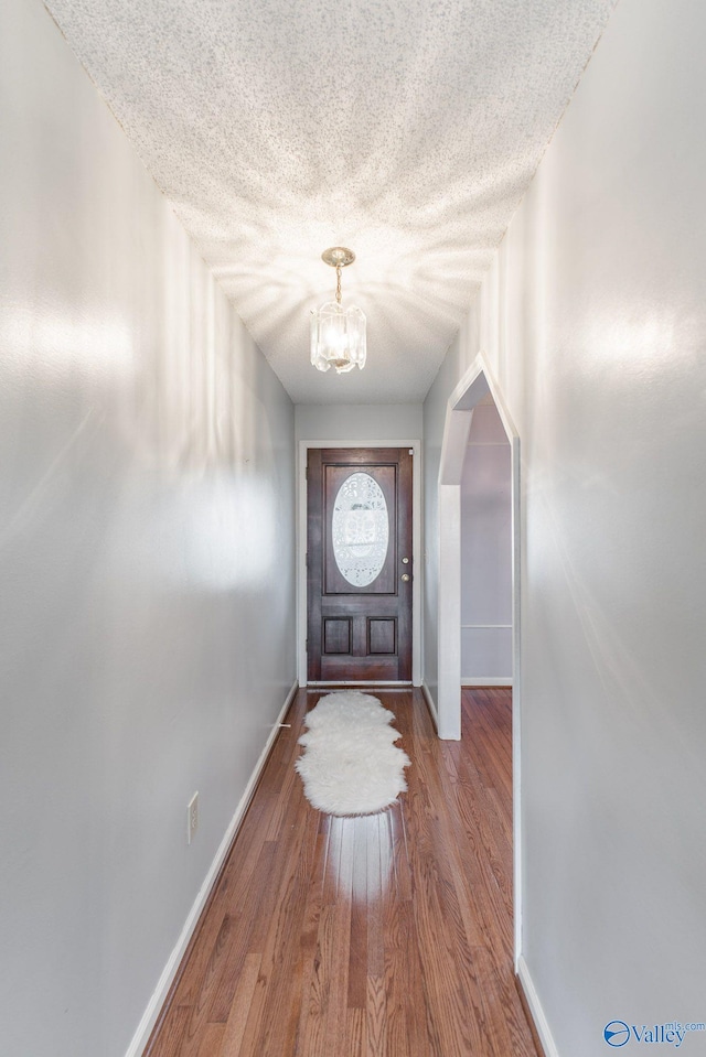 entryway featuring wood finished floors, baseboards, arched walkways, a textured ceiling, and a chandelier