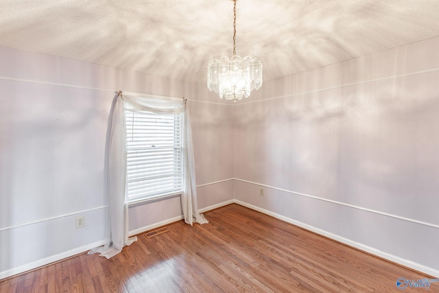 spare room with visible vents, a notable chandelier, a textured ceiling, wood finished floors, and baseboards