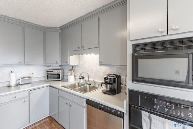 kitchen with light countertops, decorative backsplash, gray cabinets, black appliances, and a sink