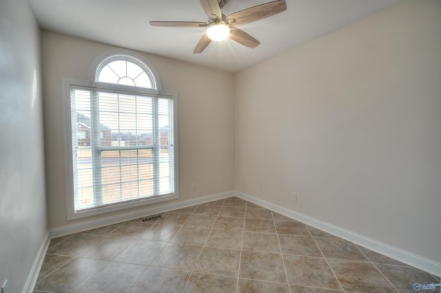 tiled empty room featuring visible vents, a ceiling fan, and baseboards