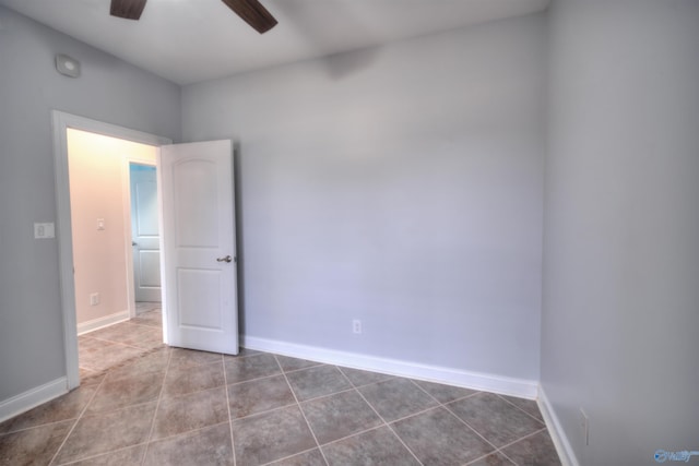 tiled empty room with ceiling fan and baseboards