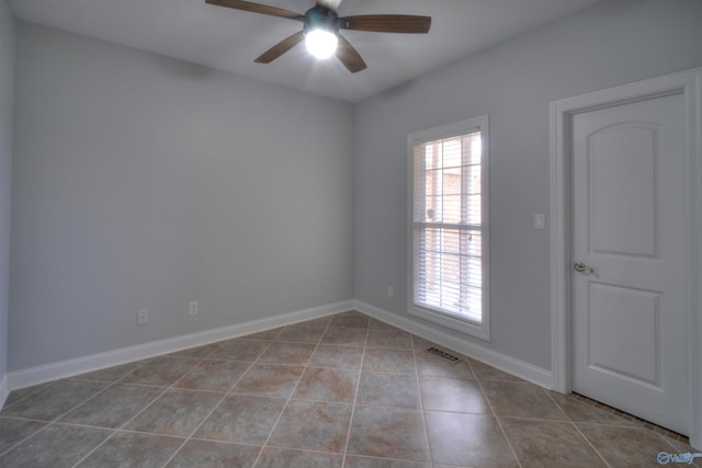 tiled empty room with baseboards, visible vents, and a ceiling fan