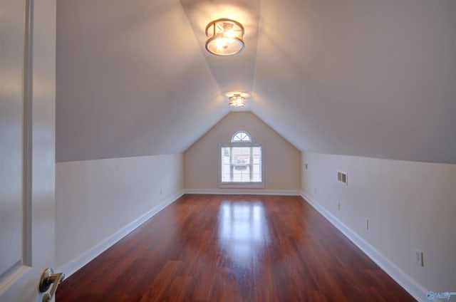 bonus room featuring dark wood finished floors, visible vents, baseboards, and vaulted ceiling