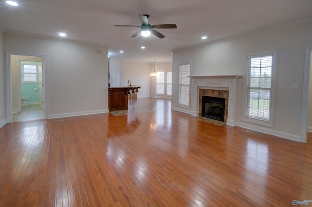 unfurnished living room featuring light wood finished floors, ceiling fan, a tiled fireplace, and a wealth of natural light