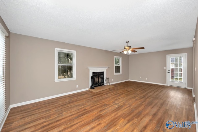 unfurnished living room featuring ceiling fan, dark wood-type flooring, and a textured ceiling