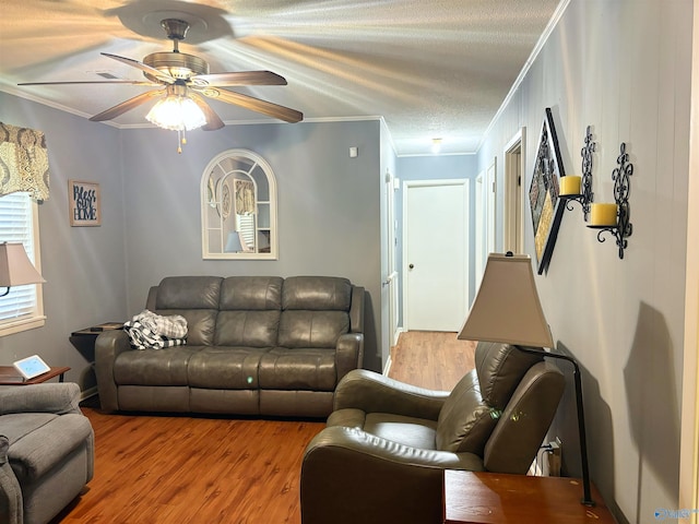 living room featuring ceiling fan, ornamental molding, a textured ceiling, and wood finished floors