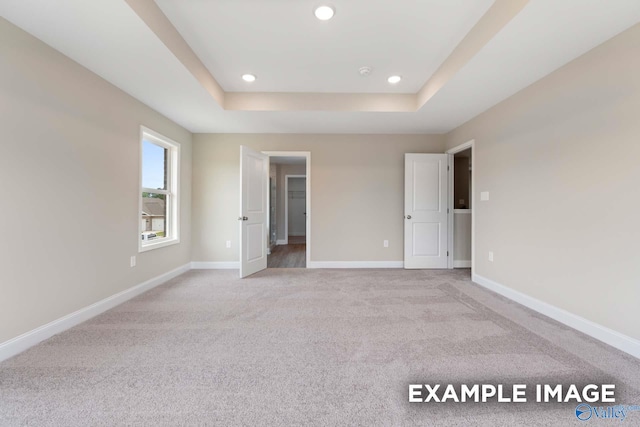 unfurnished bedroom featuring a raised ceiling and light carpet