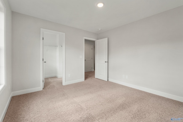 unfurnished bedroom with a walk in closet, a closet, and light colored carpet