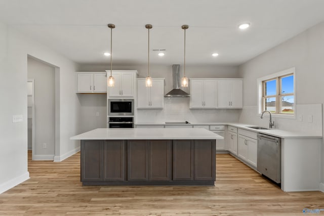 kitchen with a sink, white cabinetry, light countertops, wall chimney range hood, and appliances with stainless steel finishes