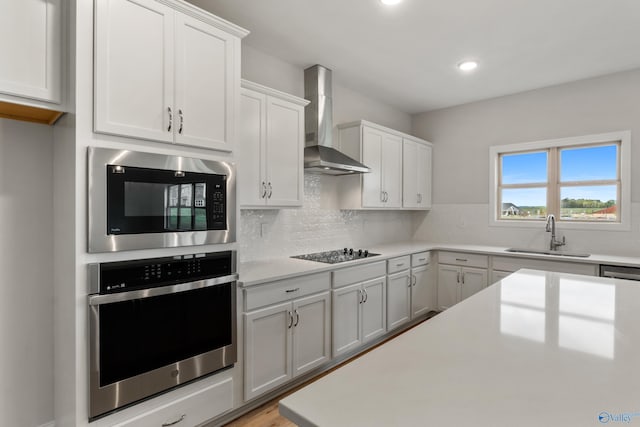 kitchen featuring a sink, white cabinetry, light countertops, wall chimney range hood, and black appliances