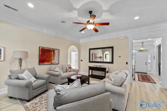 living room with arched walkways, visible vents, baseboards, ornamental molding, and light wood-type flooring