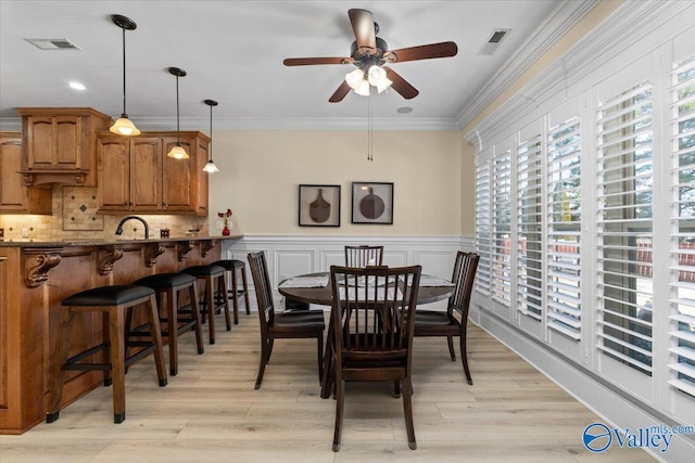 dining area with light wood-style floors, visible vents, crown molding, and wainscoting