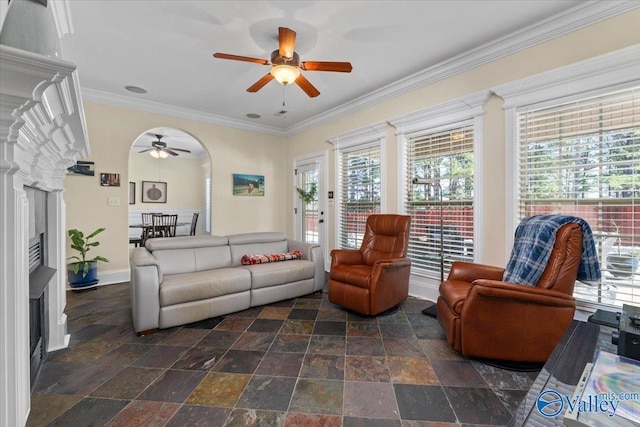 living area with arched walkways, a fireplace, ornamental molding, stone finish floor, and baseboards