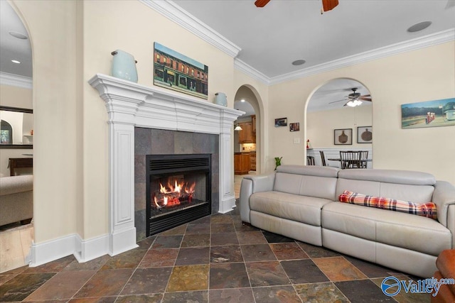 living area with stone tile flooring, crown molding, a fireplace, and a ceiling fan