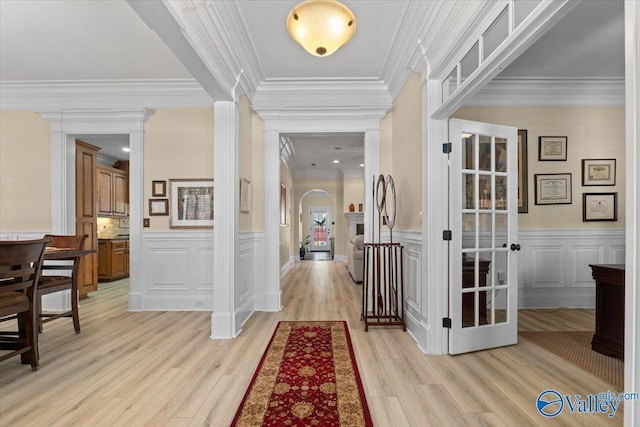 interior space with arched walkways, a wainscoted wall, light wood-type flooring, and a decorative wall