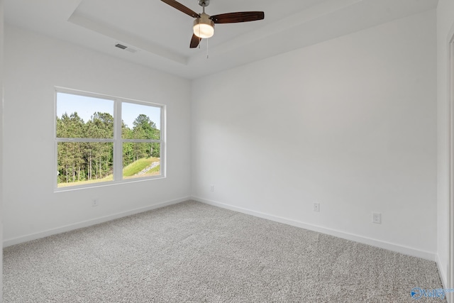 empty room featuring carpet, visible vents, a tray ceiling, and baseboards