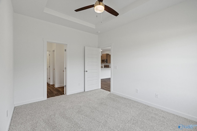 unfurnished bedroom featuring a raised ceiling, dark carpet, baseboards, and ceiling fan