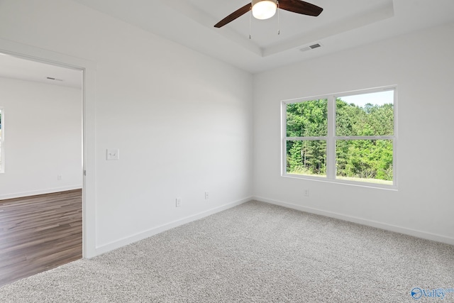 carpeted empty room with a ceiling fan, a raised ceiling, visible vents, and baseboards