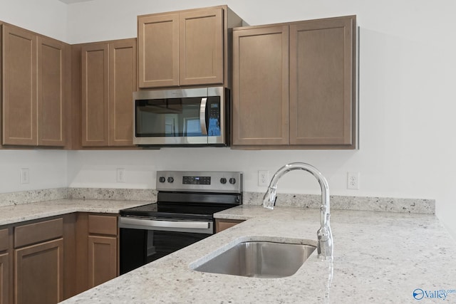 kitchen featuring appliances with stainless steel finishes, light stone counters, and a sink