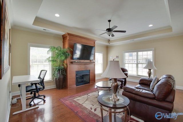 living room featuring ornamental molding, a fireplace, hardwood / wood-style floors, a tray ceiling, and ceiling fan