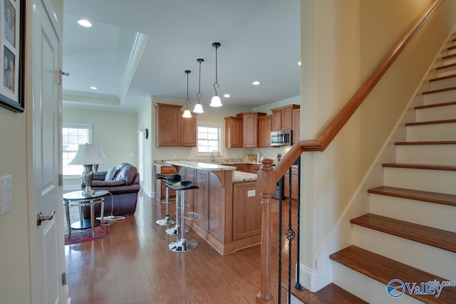 kitchen featuring a kitchen bar, a raised ceiling, light stone countertops, light wood-type flooring, and decorative light fixtures