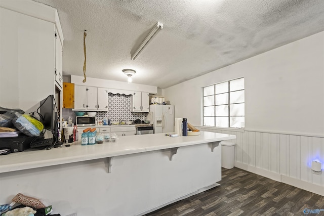 kitchen with white fridge with ice dispenser, a textured ceiling, a kitchen bar, white cabinetry, and kitchen peninsula