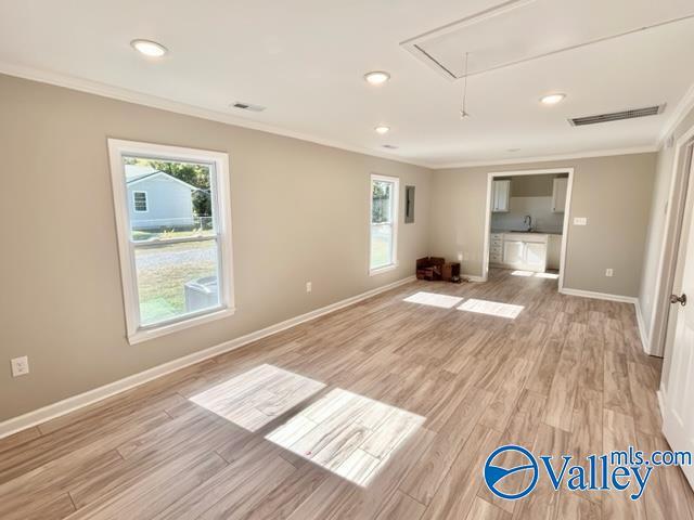 unfurnished living room featuring attic access, visible vents, light wood finished floors, and ornamental molding