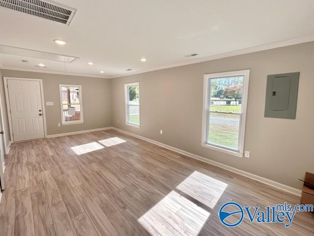 unfurnished living room with crown molding, visible vents, electric panel, baseboards, and attic access