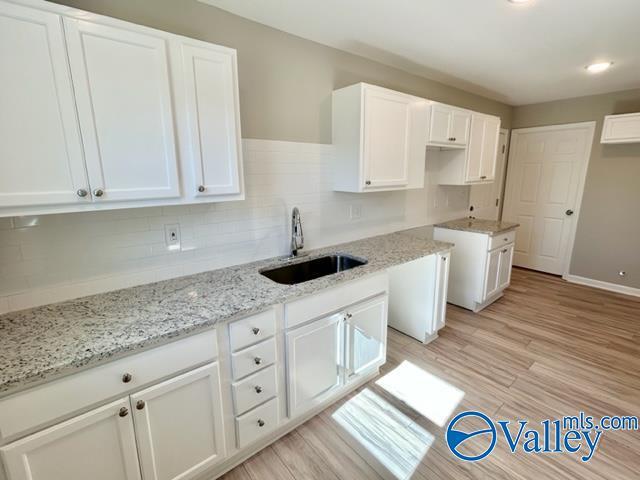 kitchen with light stone counters, backsplash, a sink, white cabinetry, and light wood-type flooring