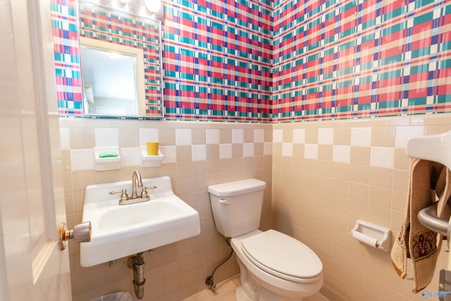 half bathroom with toilet, tile walls, a sink, and wainscoting