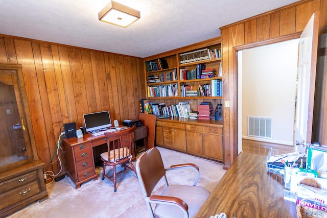 office featuring light colored carpet, visible vents, wooden walls, and a textured ceiling