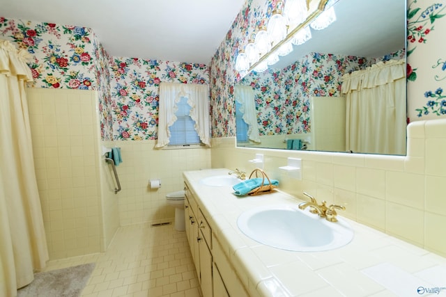 bathroom with a wainscoted wall, tile patterned flooring, a sink, and wallpapered walls