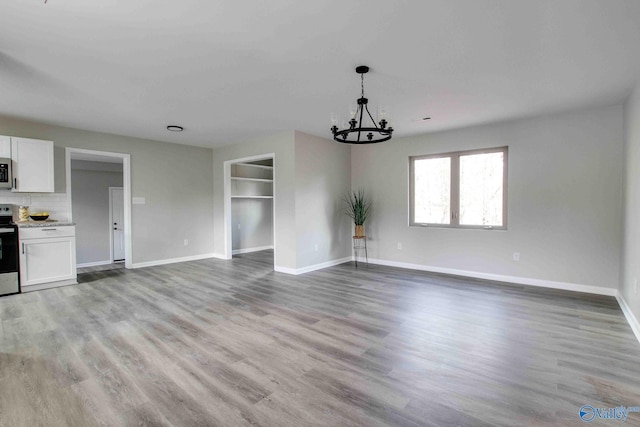 unfurnished living room featuring built in features, light hardwood / wood-style floors, and an inviting chandelier