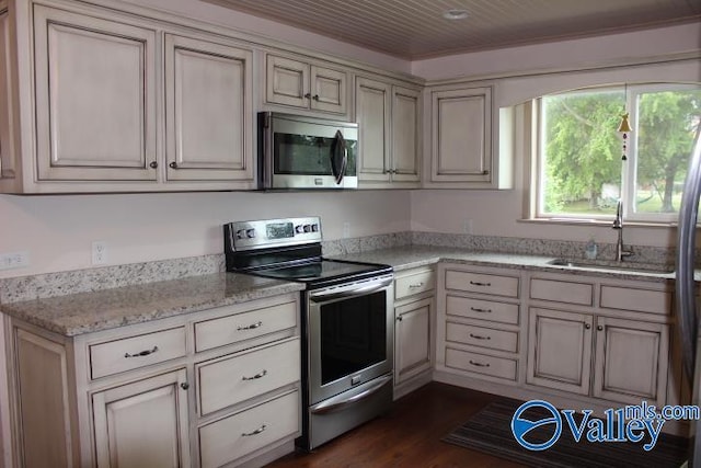 kitchen with appliances with stainless steel finishes, sink, dark hardwood / wood-style flooring, light stone counters, and cream cabinetry