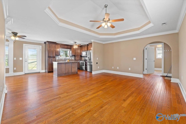 unfurnished living room featuring ceiling fan, ornamental molding, a raised ceiling, and light hardwood / wood-style flooring