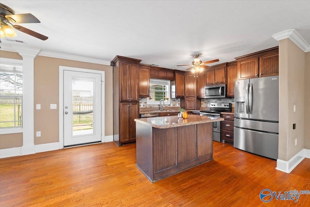 kitchen with light stone counters, appliances with stainless steel finishes, hardwood / wood-style floors, and a kitchen island